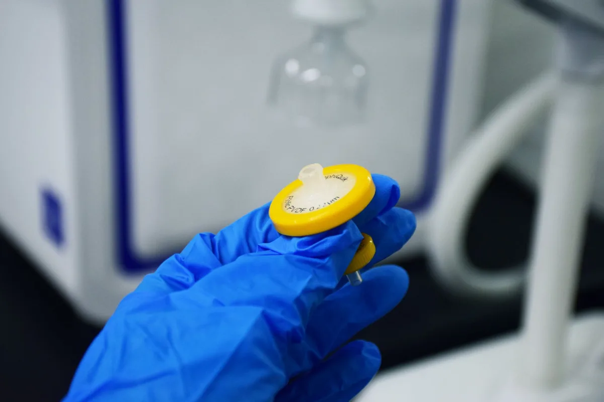Gloved hands rinsing a septic effluent filter cartridge back into the tank