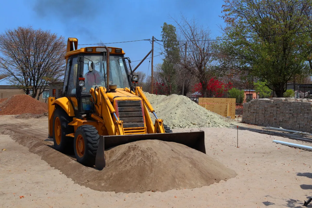 Excavator digging a trench during a septic drain field repair in a backyard
