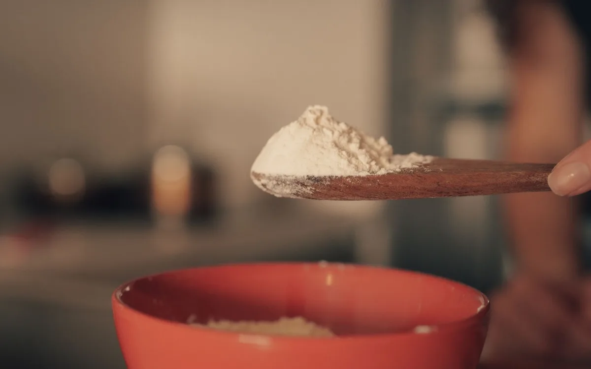 Scoop of powder dishwasher detergent held over an open detergent box