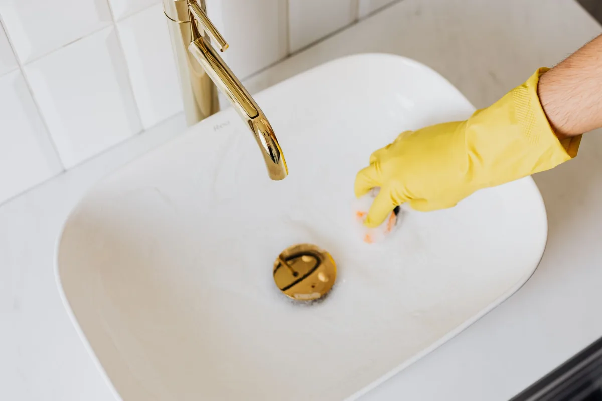 Homeowner using a plunger to clear a single slow drain in a bathroom sink