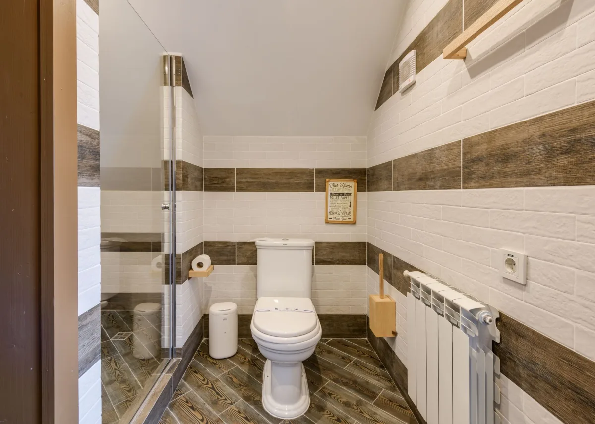 A small lidded trash can placed next to a toilet in a home bathroom