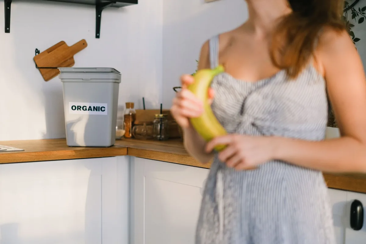 Countertop compost pail holding vegetable scraps beside a kitchen sink