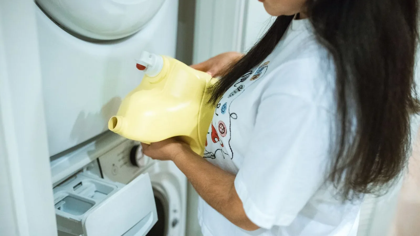 Person pouring liquid laundry detergent into a measuring cap above a washing machine